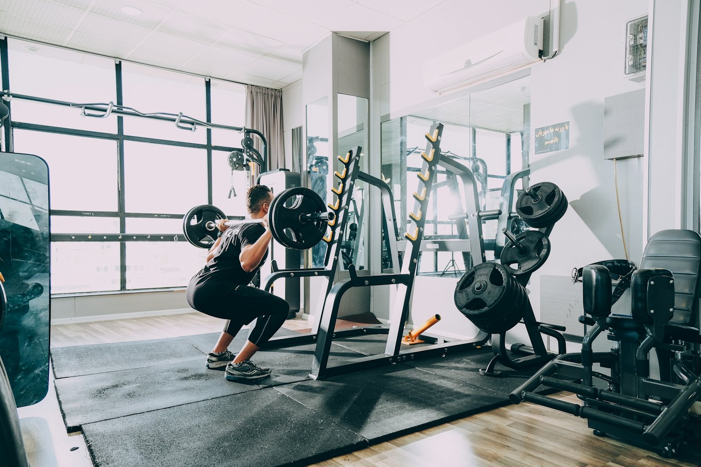 Person performing a barbell back squat in a modern gym.